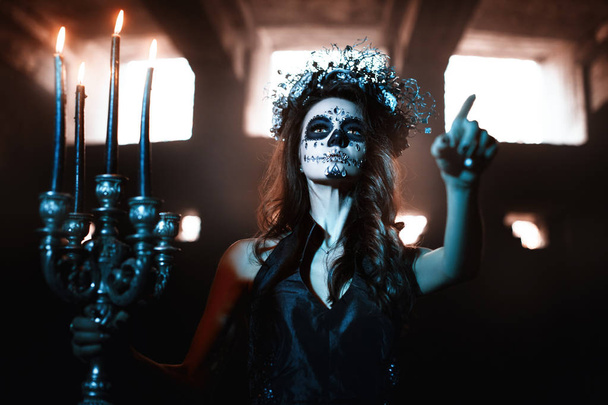 Mujer joven con maquillaje para la celebración de Halloween sosteniendo un candelero con velas encendidas
. - Foto, Imagen