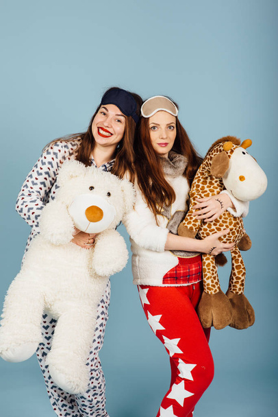 two happy girls in pajamas hold toys in their hands - Zdjęcie, obraz