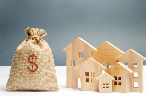Bag with money and dollar sign and wooden houses. Financing in the country. Investing money in real estate. Saving and accumulation of money. Mortgage. Buying a home. Property sale. City budget. - Foto, Imagen