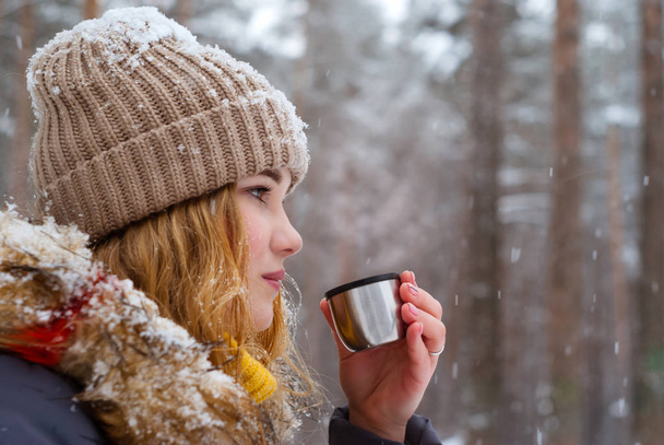 girl holds in her hand a cup of tea (thermos cap) outdoors on a frosty day - Photo, Image