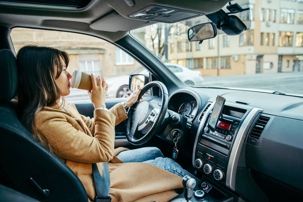 jonge mooie vrouw rijdt auto onder het genot van kopje koffie. levensstijl - Foto, afbeelding