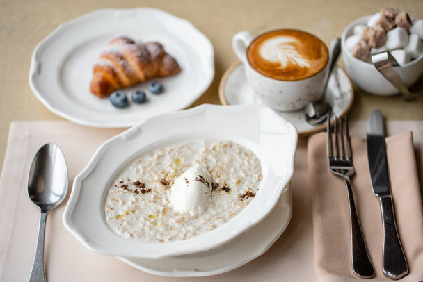 Bowl of breakfast oatmeal with soft Italian cheese and cinnamon. Croissants, coffee and other dishes on the table in the restaurant - Foto, imagen