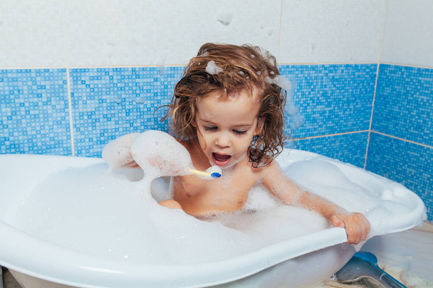 Beautiful young girl bathes in the bathroom and brushes her teeth with a toothbrush. Daily morning routines. Children's hygiene is fun. - Photo, Image