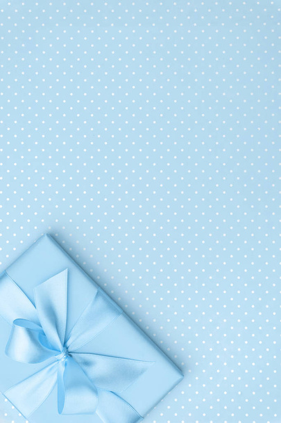 Geschenkkarton mit blauer Schleife auf blau gesprenkeltem Hintergrund von oben. Urlaubskonzept, Geburtstagsgeschenk, 8. März oder Frauentag, Geschenkbox Urlaub Muttertag. Grußkarte mit Kopierplatz. flache Lage - Foto, Bild