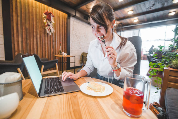 mooie vrouw overladen met werk zitten in cafe met laptop eten en drinken luisteren muziek op headset. lifestyle concept. freelance - Foto, afbeelding