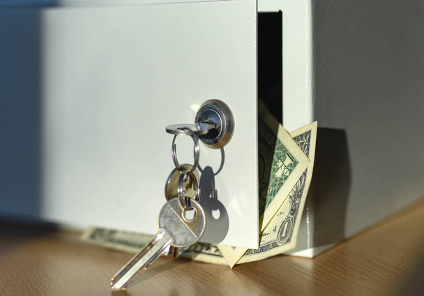 Key-opened door of a white safe with money on the office table - Фото, изображение
