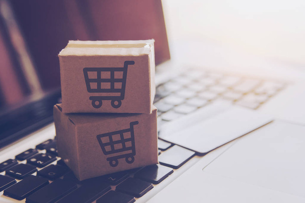 Online-Shopping-Konzept - Shopping-Service im Internet. mit Zahlung per Kreditkarte und bietet Lieferung nach Hause. Paket- oder Papierkartons mit einem Warenkorb-Logo auf einer Laptop-Tastatur - Foto, Bild