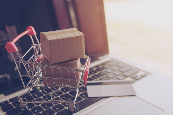 Online-Shopping-Konzept - Shopping-Service im Internet. mit Zahlung per Kreditkarte und bietet Lieferung nach Hause. Paket- oder Papierkartons mit einem Warenkorb-Logo auf einer Laptop-Tastatur - Foto, Bild