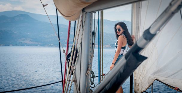 Giovane ragazza adolescente con occhiali da sole su barca a vela incorniciato da albero, boom e vang
 - Foto, immagini