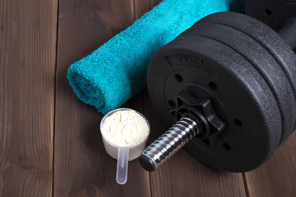 Blue towel, black dumbbell, whey protein on a wooden floor. Gym. Background Sport Fitness Bodybuilding Healthy Lifestyle and Weightlifting Concept - Foto, Imagem