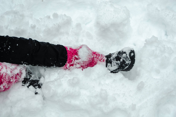 Η εφηβική κοπέλα κάθεται σε ένα πάρκο που καλύπτονται με χιόνι. Κοντινό πλάνο του κοριτσιού χιόνι που καλύπτει τα πόδια. - Φωτογραφία, εικόνα