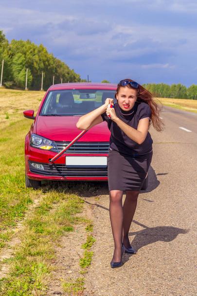 Güzel bir genç kadın bir elbise ve topuklu ayakkabılar bir araba tarafından ipi çekiyor. Kadın gücü, bağımsızlık ve azim kavramı - Fotoğraf, Görsel