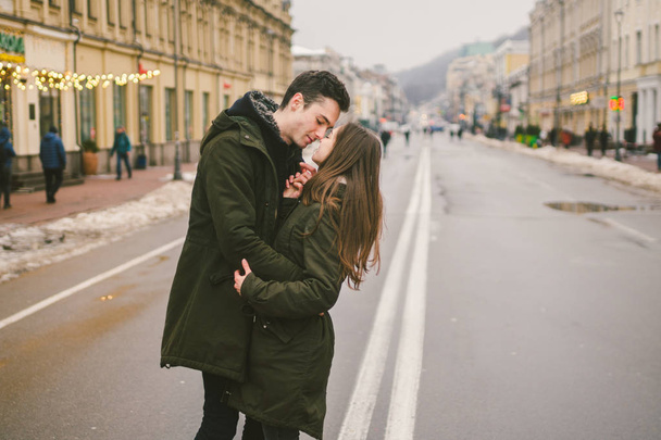 Theme love and romance. Caucasian young people heterosexual couple in love students boyfriend girl hugging and kissing on center of road in center of European city. Man woman happiness love and youth. - Фото, изображение