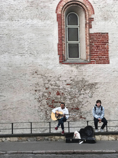 Riga, Latvia, September 18, 2018. One guy plays the guitar and sings a romantic song, the second one listens. Near the case from the guitar, where passers-by throw money. Nearby is a high brick wall.  - Photo, Image