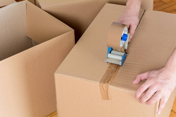 Man sealing a shipping cardboard box with tape dispenser. Indoors - Fotoğraf, Görsel