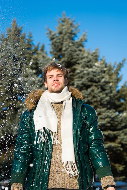 Winter fashion concept. Guy enjoy sunny winter day. Hipster walk snowy winter day. Snowflakes in air on bright winter day. Man unshaven wear warm jacket with fur and scarf snowy nature background - Foto, Imagen