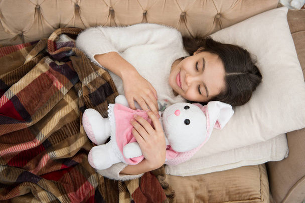 Play soft toy before go sleep. Sleep with toy. Girl enjoy evening time with favorite toy. Kid lay bed and hug bunny toy couch pillow blanket background top view. Girl child wear pajamas hug bunny - Photo, image
