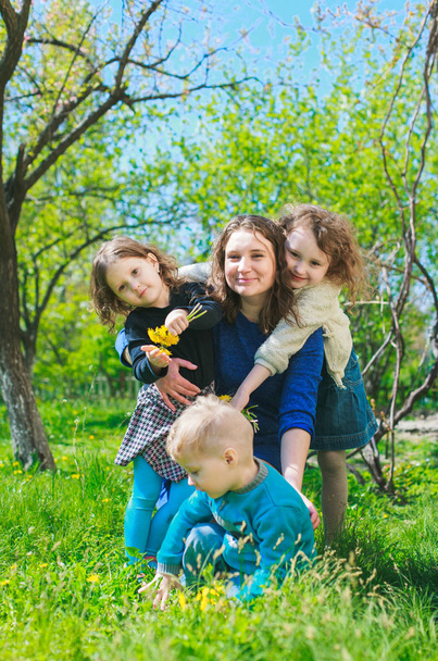 Mama z trojgiem dzieci - chłopiec i dwie dziewczynki uśmiechnięte, a jej dzieci się przytulają. Szczęśliwa duża rodzina w przyrodzie. - Zdjęcie, obraz