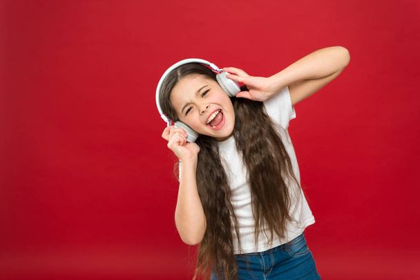 Modern gadget concept. Music taste. Music plays an important part lives teenagers. Powerful effect music teenagers their emotions, perception of world. Girl listen music headphones on red background - Photo, Image