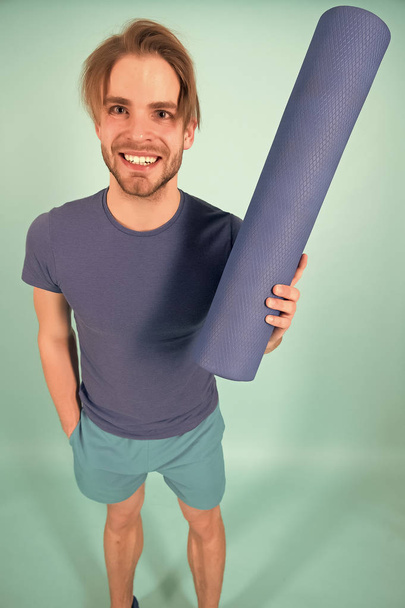 Happy sportsman smile with yoga mat. Fashion athlete in blue tshirt and shorts. Man with stylish bristle and hair. Gym equipment for training and workout. Yoga or pilates and sport activity - Fotó, kép