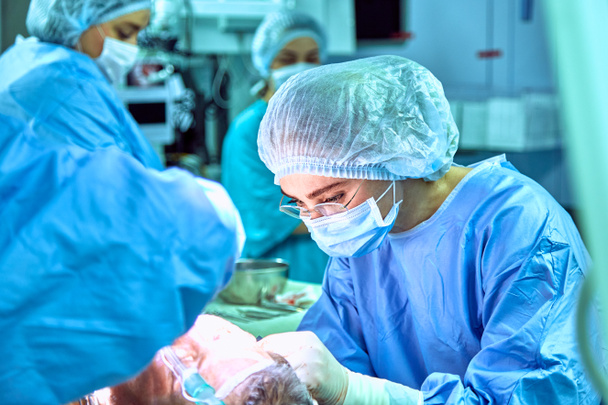 Useat kirurgit ympäröivät potilasta leikkauspöydällä työnsä aikana
 - Valokuva, kuva