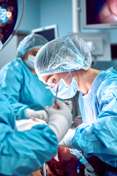 Varios cirujanos que rodean al paciente en la mesa de operaciones durante su trabajo
 - Foto, Imagen