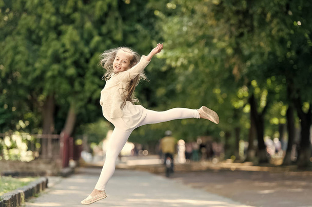 Child happy and cheerful enjoy walk in park. Happiness concept. Kid gymnast with cheerful expression jumps up on international childrens day. Girl on happy smiling face jumps, nature on background - Zdjęcie, obraz