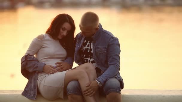 W ciąży rodzice siedzący na molo, jezioro o zachodzie słońca i ogarnięcie żołądka. - Materiał filmowy, wideo