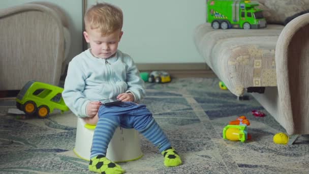 Adorable boy with a smartphone during potty training on the room. - Imágenes, Vídeo