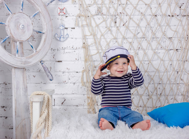 Portrait of a cute and naughty european little girl in a sailors clothing in the studio of marine style on a background of white brick wall - Photo, Image