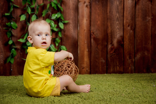 Portrait of a cute little european girl sitting in the yellow shirt on a green carpet in the studio with the brown background of wooden boards - Foto, Imagem
