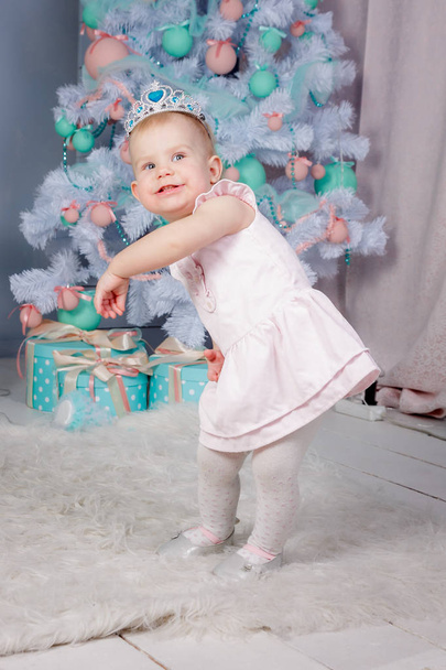 Portrait of a cute little european blond princess girl with a crown  in a beautiful dress in a studio decorated in the Christmas theme with toys and christmas tree - Фото, зображення