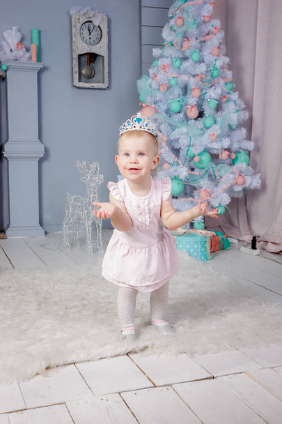 Portrait of a cute little european blond princess girl with a crown  in a beautiful dress in a studio decorated in the Christmas theme with toys and christmas tree - Foto, immagini