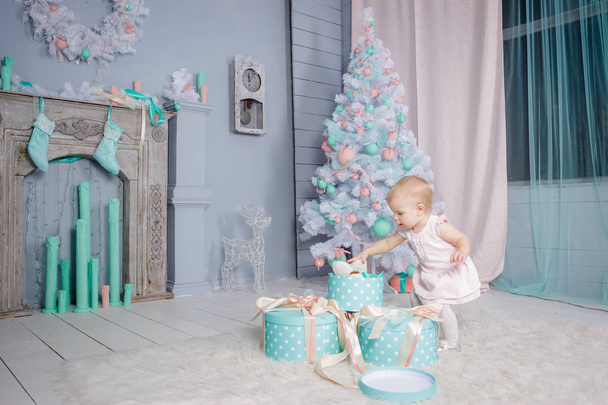 Portrait of a cute little european blond princess girl with a crown  in a beautiful dress opening gifts in a studio decorated in the Christmas theme with toys and christmas tree - Foto, immagini
