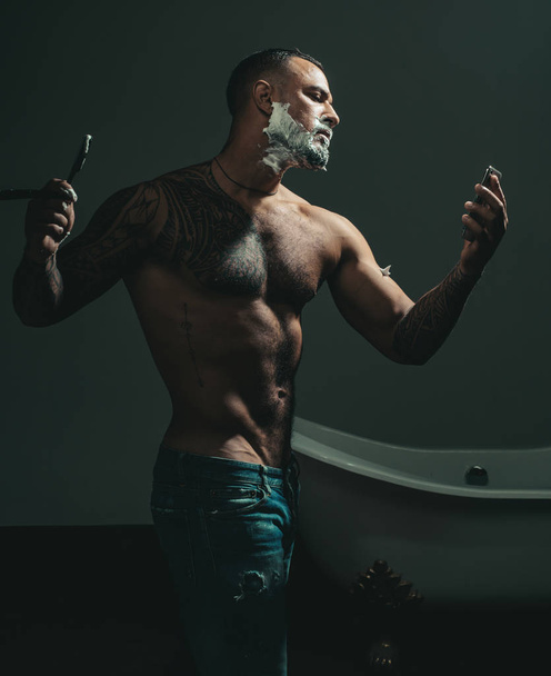 Hairdressers work for a handsome guy at the barber shop. Man visiting hairstylist in barber shop. Beard balm. Shaving man and razor man. Barber shaving a bearded man in a barber shop. - 写真・画像