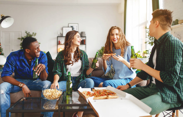 group of happy young  friends with beer and pizza at home - Foto, afbeelding