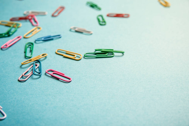 Colored paperclips randomly arranged on blue paper with copy space. - Foto, immagini