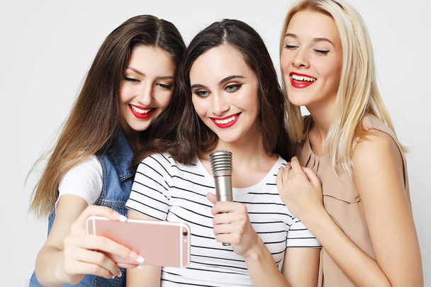 Mikrofonlu iki güzel kız akıllı telefonlu selfie çekiyor.  - Fotoğraf, Görsel