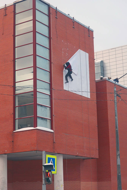 Escalador industrial desmantelando bandera blanca de la pared de ladrillo rojo
 - Foto, Imagen