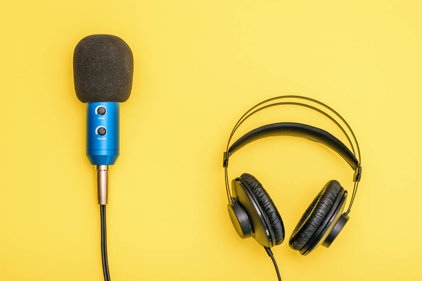 黒のヘッドフォンと明るい黄色の背景に青いマイク。記録、通信、音楽を聴くのための機器. - 写真・画像
