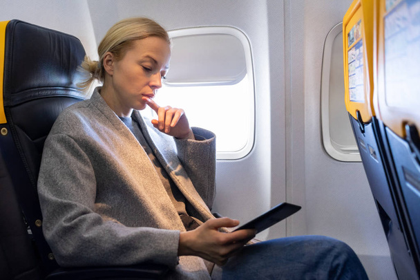 Жінка читає на цифровому електронному пристрої читання під час подорожі літаком
. - Фото, зображення
