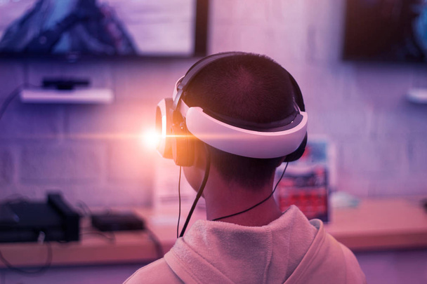 Νεαρό gamer φορώντας Vr γυαλιά και ακουστικά παίζει, νικητή οδηγό και καθαριστή online παιχνίδι βίντεο στον υπολογιστή του προσωπικού στην αίθουσα φωτίζεται από φώτα νέον. VR, esport δίκτυο online. - Φωτογραφία, εικόνα