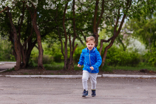 six-year-old Caucasian boy in a blue windbreaker and gray pants running in the Park in the spring - Photo, image