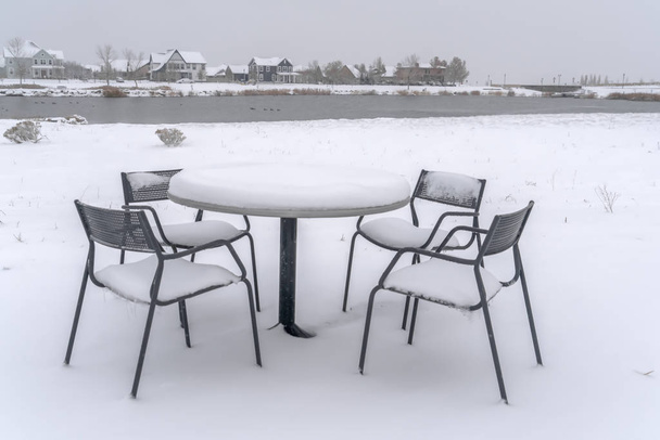 verschneiter Tisch und Stühle am Seeufer bei Tagesanbruch - Foto, Bild
