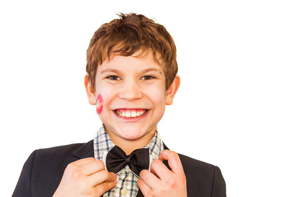 Teenager Junge mit Lippenstift-Print auf Wange richtet Fliege auf weißem Hintergrund - Foto, Bild