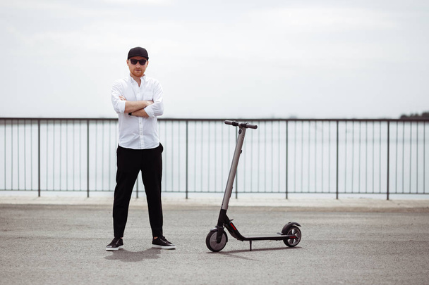 Modern man dressed white shirt and black pants standing at the street with electric scooter - Foto, Bild
