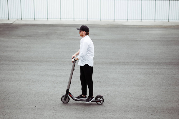Modern man in stylish black and white outfit riding electric scooter in the city - Фото, зображення