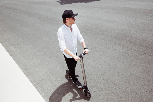 Modern man in stylish black and white outfit riding electric scooter in the city - Photo, image