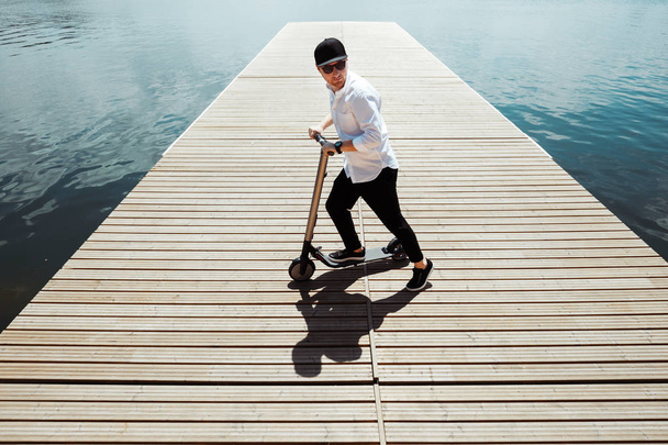 Photo of modern man with electric scooter at a wooden pier - Foto, Imagem