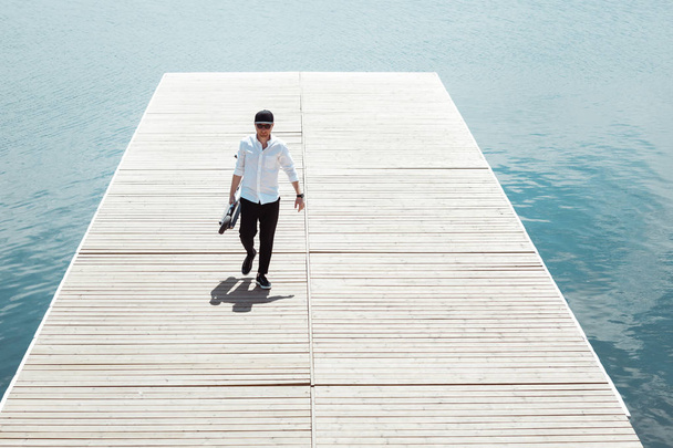 Photo of modern man with electric scooter at a wooden pier - Photo, Image